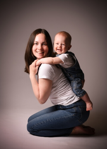 Leende mamma med sitt barn på ryggen i fotostudio, porträttfotografering.